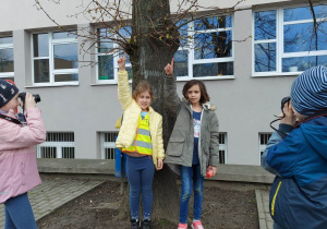Uczennice wskazują pąki na drzewach, które fotografują uczniowie