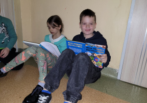 Uczeń i uczennica czytają książki na korytarzu.