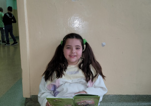 Uczennica siedzi i czyta książkę na we wnęce na korytarzu szkolnym.