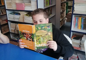 Uczeń siedzi przy stoliku w bibliotece szkolnej i czyta książkę.
