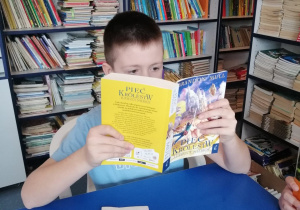 Uczeń siedzi przy stoliku w bibliotece szkolnej i czyta książkę.
