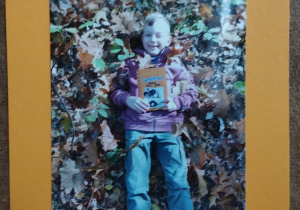 fotografia przedstawiająca chłopca, który leży w liściach i trzyma książkę w rękach