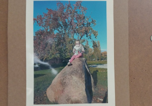 fotografia z dziewczynką, która siedzi na ogromnym kamieniu w parku i czyta książkę