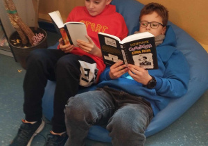 uczniowie siedzą na pufie i czytają książki